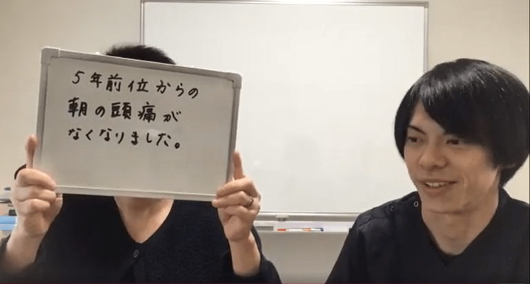 「5年前位からの朝の頭痛がなくなりました」と書かれたホワイトボードを持つ利用者と、それを見守る施術者。